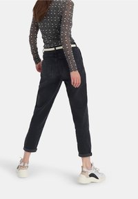 Musta korkeavyötäröinen farkut rento istuvuus, käännetyt lahkeet ja takataskut, yhdistettynä kuviolliseen pitkähihaiseen paitaan ja kevyisiin tennareihin.