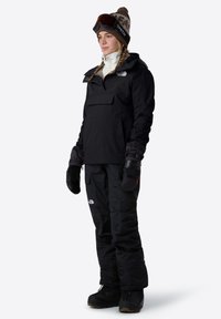 Černá vodotěsná lyžařská bunda s přední kapsou, spárovaná s zateplenými černými kalhotami, rukavicemi a zimními botami, s hnědou vzorovanou čepicí.