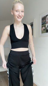 Top cropped preto com decote V profundo e textura canelada, combinado com calças de moletom pretas com riscas brancas laterais. Design simples, tecido suave.