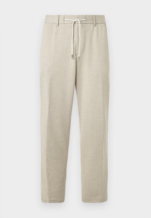 Jasnobeżowe sportowe spodnie z elastycznym pasem, sznurkiem do regulacji i ściągaczami przy kostkach, wykonane z miękkiego, teksturowanego materiału.