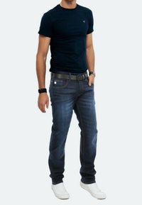 T-shirt a maniche corte blu navy, jeans in denim, cintura nera e sneakers bianche. I jeans hanno una vestibilità classica e un leggero sbiadimento.