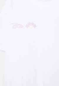 T-shirt blanc avec un petit texte rose « Design Studios 2020 » et cinq étoiles disposées en arc sur la partie supérieure gauche de la poitrine.