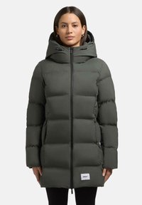 Polstret parka-jakke i mørk olivengrøn med lynlås foran, justerbar hætte og sidelommer. Funktioner et logo-patch ved kanten.