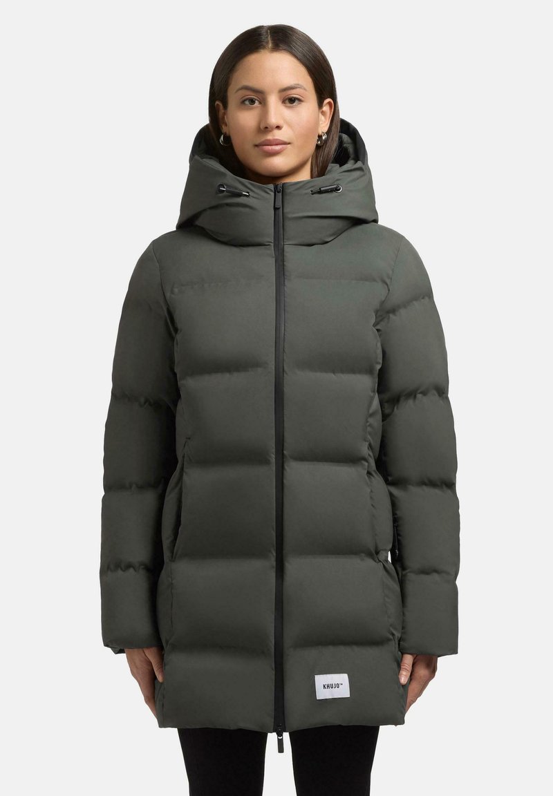 Polstret parka-jakke i mørk olivengrøn med lynlås foran, justerbar hætte og sidelommer. Funktioner et logo-patch ved kanten.