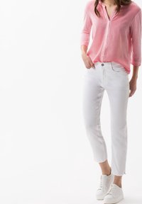 Růžová košile s dlouhým rukávem a zapínáním na knoflíky, doplněná přiléhavými bílými džíny a bílými teniskami. Jednoduchý design s hladkou tkaninou.