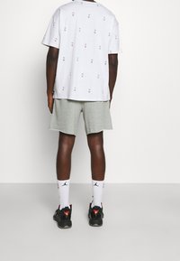 Szara koszulka z krótkim rękawem z powtarzającym się małym nadrukiem logo NBA, zestawiona z jasnoszarymi szortami. Czarne sneakersy i białe skarpetki z logo Jordan.