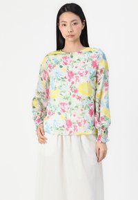 Blouse florale avec imprimé multicolore en rose, jaune et bleu. Tissu léger, manches longues avec poignets froncés, col rond.