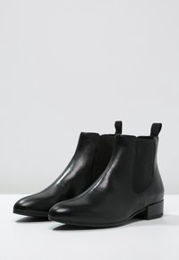 Botines de cuero negro con un acabado pulido, inserciones elásticas en los laterales, punta afilada y tacón bajo en bloque. Diseño simple y elegante.