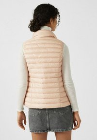 Light pink puffer vest with horizontal quilted design, high collar, and zip closure, paired with a textured white long-sleeve top and gray denim skirt.