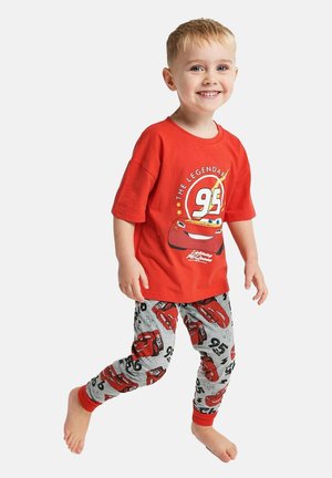 Junger Junge, der lächelt und barfuß läuft, trägt ein rotes Lightning McQueen T-Shirt und passende graue Leggings mit roten Auto-Motiven.