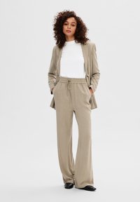 Lichtbeige blazer en bijpassende wijde broek met een trekkoord in de taille, over een wit T-shirt met ronde hals, gecombineerd met zwarte schoenen.