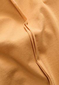 Tissu en coton de couleur pêche clair avec détails de couture visibles. La texture lisse est légèrement étirée, mettant en valeur un design doux et décontracté.