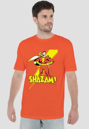 Man wearing an orange T-shirt with a Shazam comic character and yellow lightning bolt graphic on the front.