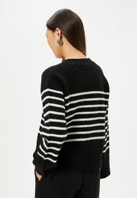 Schwarz-weißer gestreifter Pullover mit weicher Textur, der horizontale Streifen und einen runden Halsausschnitt hat. Lange Ärmel und lockere Passform.