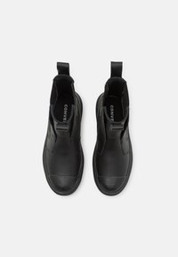 Botas de tobillo de cuero negro con paneles elásticos en los lados, punta redondeada y lengüetas de tirón. Textura suave con puntera reforzada y diseño minimalista.