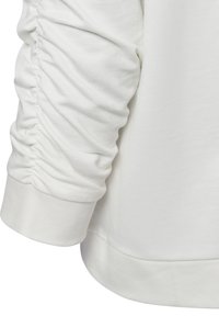 Witte langemouwen top met geplooide details langs de mouwen en een geribbelde manchette bij de pols, gemaakt van zachte stof.