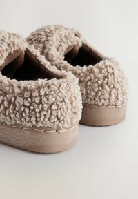 Beige slip-on sko med en tekstureret, fluffy overdel og en glat gummisål. Udsparingsdesign foran for åndbarhed.
