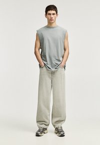 Grijze mouwloze katoenen top, lichtgrijze wijde denim jeans en grijze sneakers met zwarte accenten. Casual outfit met een ontspannen pasvorm.