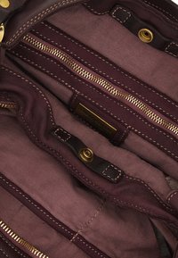 Interni bordeaux di una borsa a mano con molteplici scomparti con zip, dettagli in metallo dorato e accenti cuciti, realizzata in un tessuto resistente.