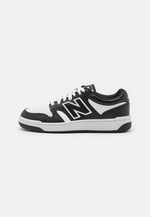 Baskets noir et blanc avec une tige en cuir, zone de orteil perforée, logo "N" en évidence, lacets plats et semelle en caoutchouc robuste.