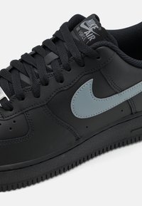 Czarny skórzany sneaker z szarym logo Nike, czarnymi sznurówkami i gumową podeszwą. Zawiera detale przeszyć oraz wyściełany kołnierz dla komfortu.