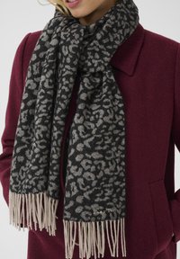 Black and gray leopard print scarf made of soft fabric, featuring cream-colored fringes at the ends. Logo visible near the fringe.