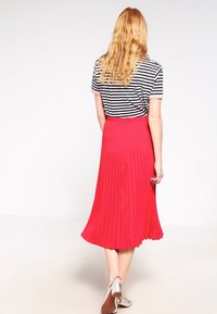 Falda midi plisada roja con una cintura ajustada, combinada con una camiseta de rayas en blanco y negro. Zapatos plateados completan el atuendo.