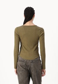 Olivenfarget langermet topp med en tettsittende ribbestruktur og rund hals, kombinert med høydeisk grå denimjeans med baklommer.