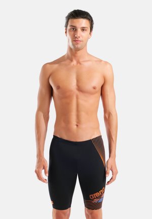 Schwarze Badehose mit orangefarbenen Akzenten und diagonalen Streifen, gefertigt aus einem glatten, elastischen Material. Für sportliche Aktivitäten konzipiert.