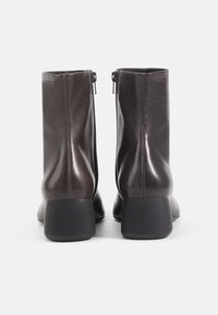 Brown leather ankle boots with a smooth texture, zip closure at the back, and a block heel, featuring a minimalist design and rounded shape.
