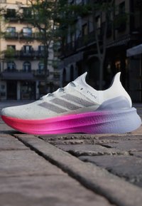 Scarpa da corsa bianca con strisce grigie, caratterizzata da una suola sfumata da rosa a viola. Upper testurizzato per traspirabilità. Design leggero.