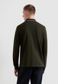 Langarm-Polohemd aus dunkelgrüner Baumwolle, mit einem klassischen Kragen und einem weißen Streifendetail, sowie einem lockeren Schnitt mit geradem Saum.
