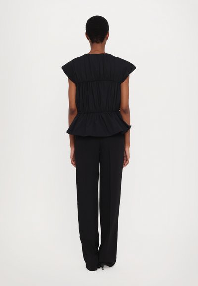Schwarzes Peplum-Top mit geraffter Textur, kurzen Puffärmeln und tailliertem Bund. Kombiniert mit schwarzen, weiten Hosen. Glattes Material.