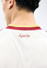 Achterkant van een persoon die een wit shirt draagt met een rood-gele kraag, "España" in rood gedrukt op de bovenrug.