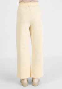 Wijdvallende broek van zacht, lichtgeel stof met een elastische tailleband en een gladde textuur, gecombineerd met beige plateau schoenen.