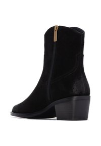 Botín de ante negro con cremallera lateral, parte superior curva y tacón bajo en bloque. Parte superior texturizada con un acento brillante en el tacón.