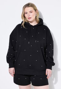Sudadera negra con capucha y adornos blancos dispersos, que cuenta con un bolsillo frontal, mangas largas y un corte relajado.