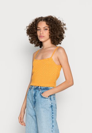 Top crop com padrão xadrez amarelo e alças finas, combinado com jeans de cintura alta em azul-claro. Textura suave, design ajustado.