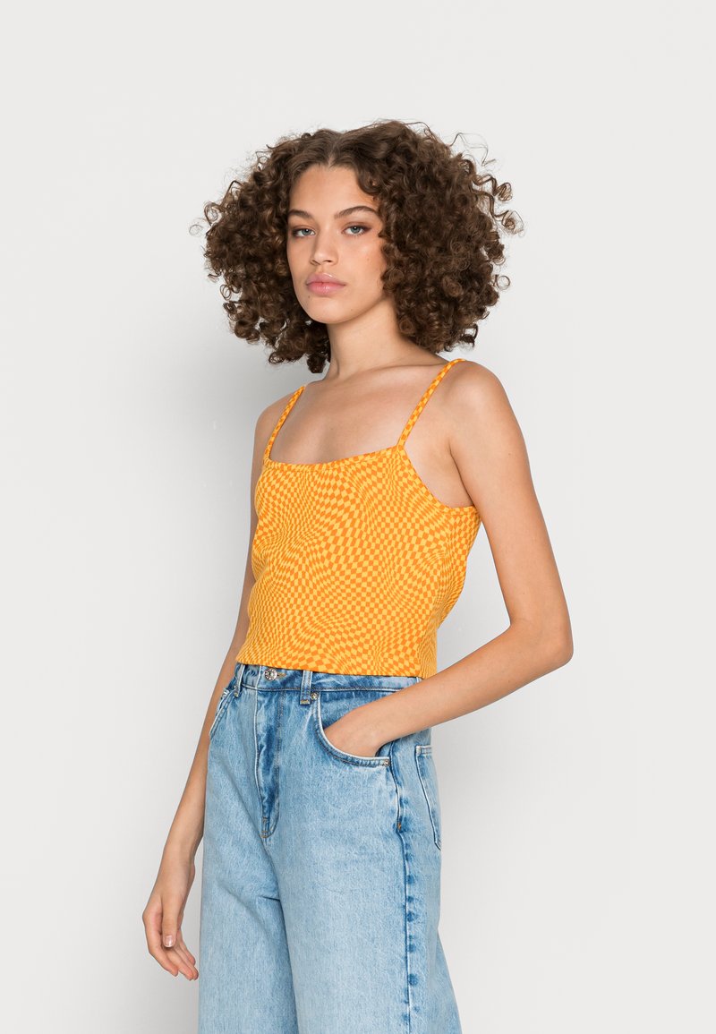 Top crop com padrão xadrez amarelo e alças finas, combinado com jeans de cintura alta em azul-claro. Textura suave, design ajustado.