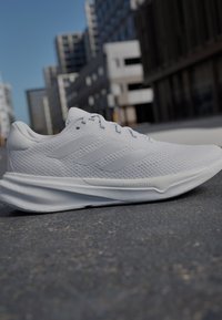 Zapatillas deportivas blancas con una parte superior de malla texturizada, un diseño de tres rayas prominente y una suela acolchada. Detalle notable del logo "DREAMSTRIKE+".
