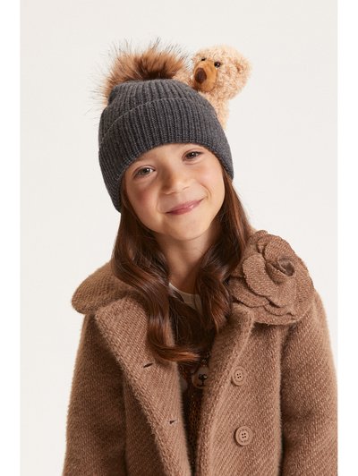 Gorro de punto gris con un pom-pom esponjoso y un acento de oso juguetón, combinado con un abrigo de doble faz de un marrón claro y texturizado con detalles florales.