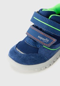 Granatowe trampki wykonane z siateczki i zamszu, z neonowymi zielonymi akcentami, pomarańczowym przeszyciem oraz regulowanymi rzepami. Jasnoszara podeszwa.