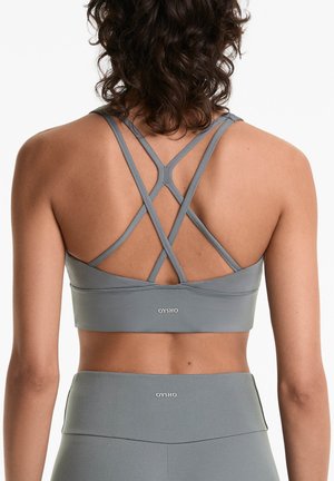 Grauer Sport-BH mit gekreuzten Trägern auf dem Rücken, aus glattem, dehnbarem Material. OYSHO-Logo am unteren Ende sichtbar.