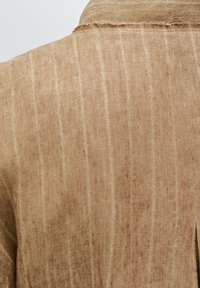 Tissu en lin beige avec des rayures verticales et une texture douce, présentant un col légèrement effiloché et un design à coupe décontractée.