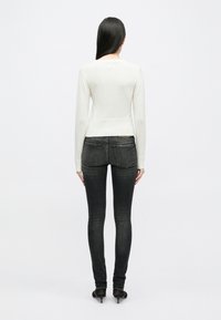 Κρεμ μπλούζα πλεκτή με στρογγυλή λαιμόκοψη, ριγέ μανίκια και στρίφωμα, σε συνδυασμό με σκούρο γκρι skinny τζιν που δείχνει ελάχιστες ραφές.
