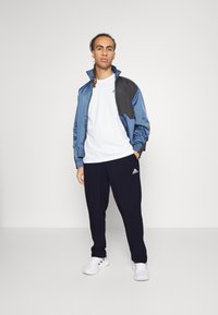 Sininen ja musta treenitakki, valkoinen T-paita, tummansiniset housut ja valkoiset lenkkarit. Ominaisuuksiin kuuluu urheilullinen muotoilu, joustavuus hihansuissa ja brändätyt yksityiskohdat.