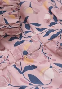 Primo piano di un tessuto rosa con stampa floreale blu e gialla e dettaglio di cuciture arricciate.