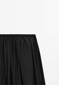 Jupe noire avec ceinture élastique froncée, confectionnée en tissu léger, présentée sur un fond blanc uni.