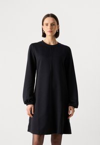 Zwart jurk met lange mouwen, een ronde halslijn, een losse pasvorm en verzamelde mouwen. Gemaakt van zachte stof met minimale stikdetails.