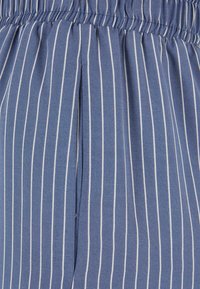 Tissu rayé bleu et blanc avec des lignes verticales, doté d'une taille élastique et d'un détail de pli sur le devant. Texture douce.